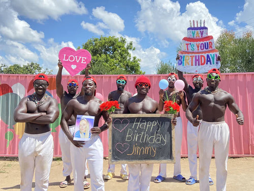 African fitness team members smiling and holding a birthday message board during a workout.