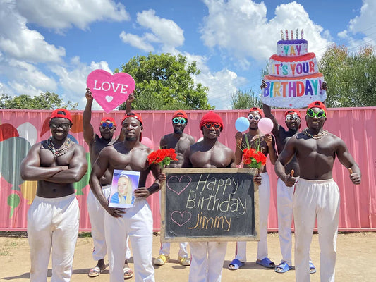 African fitness team members smiling and holding a birthday message board during a workout.