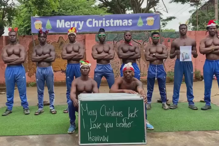 African muscle team performing a funny holiday dance with Santa hats and a custom message board